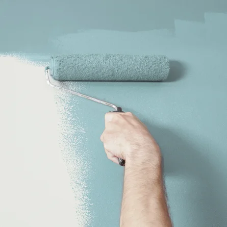 Verarbeitung - Maler streicht eine Wand mit einer Farbrolle in blauer Farbe.